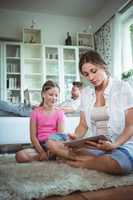 Mother and daughter sitting on floor and using digital tablet