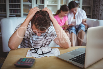 Worried man sitting at table with bills and laptop