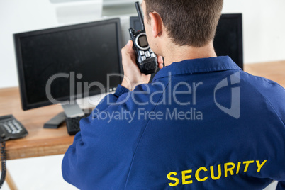 Security officer talking on walkie-talkie while looking at computer monitors