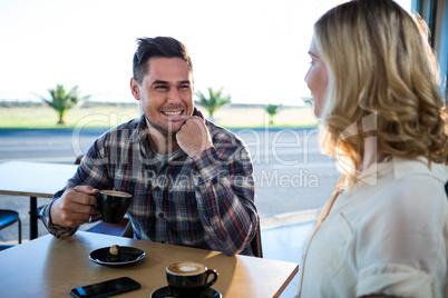 Smiling couple interacting with each other while having cup of coffee