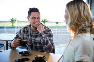 Smiling couple interacting with each other while having cup of coffee