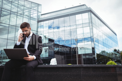 Businessman using laptop while talking on phone