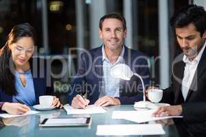 Businessman smiling at camera while colleagues writing on paper