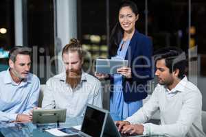 Businesswoman smiling at camera while colleagues discussing over digital tablet and laptop