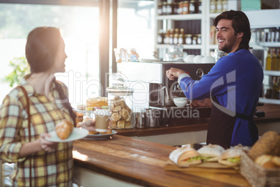 Waiter making cup of coffee while interacting with customer