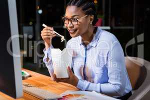 Businesswoman eating noodles at her desk