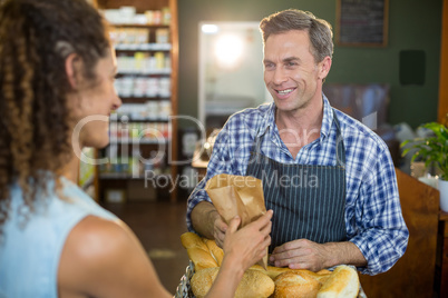 Smiling male staff giving packed bread to woman