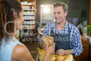 Smiling male staff giving packed bread to woman
