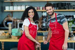 Portrait of smiling waiter and waitress leaning at counter