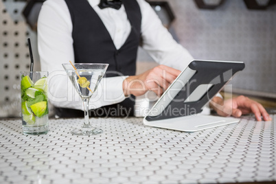 Bartender using digital tablet at bar counter