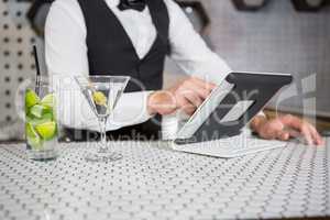 Bartender using digital tablet at bar counter