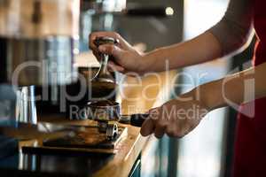 Waiter using a tamper to press ground coffee into a portafilter