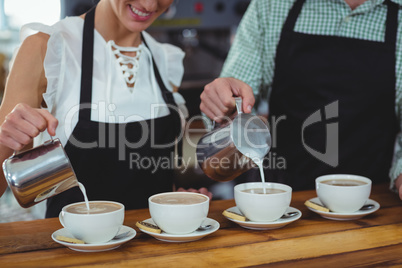 Mid section of waiter and waitress making cup of coffee at counter