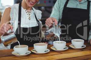 Mid section of waiter and waitress making cup of coffee at counter