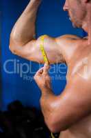 Shirtless athlete measuring biceps in gym