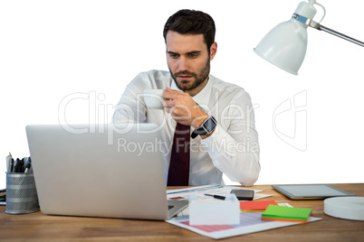 Businessman working on laptop in office while having coffee