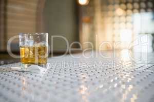 Glass of whisky with ice cube on bar counter