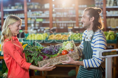 Male staff giving a crate of fresh vegetables to woman in organic section