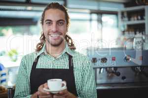 Portrait of smiling waiter holding cup of coffee