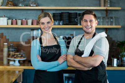 Portrait of smiling waiter and waitress standing with arms crossed