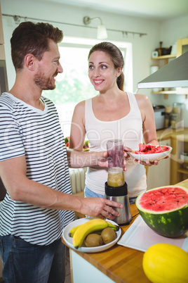 Smiling couple preparing fruit smoothie in kitchen