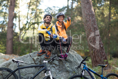 Biker couple sitting on rock and pointing in distance