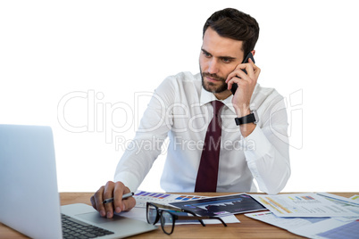 Businessman talking on mobile phone while working on laptop