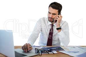 Businessman talking on mobile phone while working on laptop