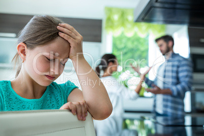 Sad girl leaning on chair while parents arguing in background