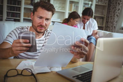 Worried man calculating bills while his wife and daughter sitting on sofa