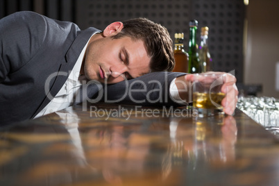Drunk man lying on a counter with glass of whisky