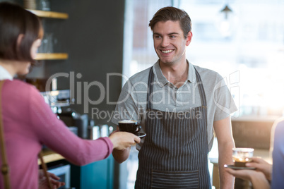 Waiter serving a cup of coffee to customer at counter