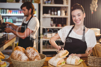 Portrait of waitress standing at counter with sandwiches and bread roll