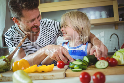 Father and daughter smiling at each other while preparing salad