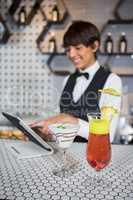 Waitress using digital tablet with glass of cocktail in bar counter