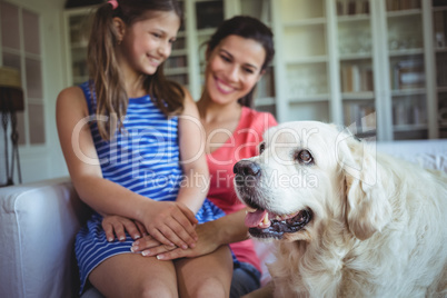 Mother and daughter sitting with pet dog in living room