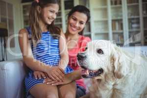Mother and daughter sitting with pet dog in living room