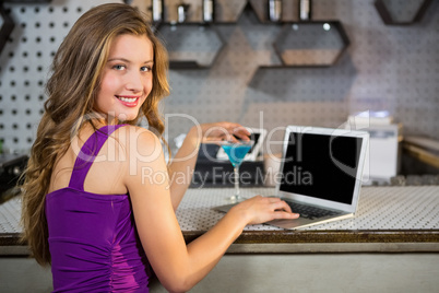 Beautiful woman using laptop while having cocktail