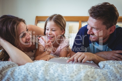 Parents lying with daughter on bed and looking at photo album