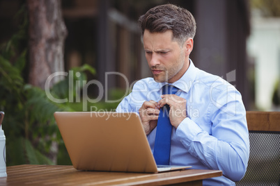 Handsome businessman adjusting tie while using laptop