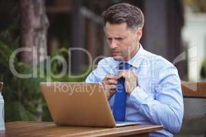 Handsome businessman adjusting tie while using laptop
