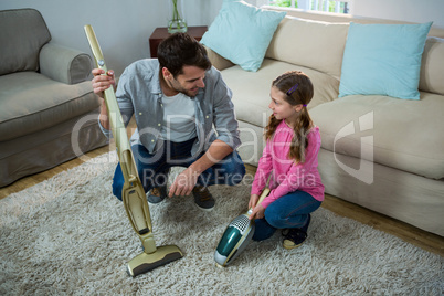 Daughter helping father to clean carpet with a vacuum cleaner