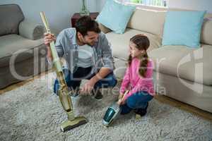 Daughter helping father to clean carpet with a vacuum cleaner