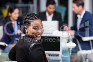 Businesswoman smiling at camera while colleagues interacting in the background