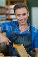 Portrait of smiling male staff packing bread in paper bag