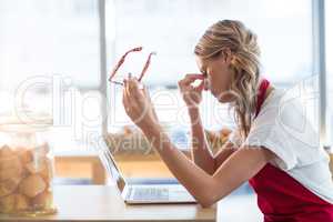 Waitress sitting at table and using laptop in cafÃ?Â©
