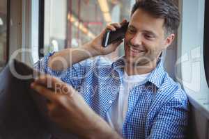 Handsome man holding newspaper while talking on mobile phone