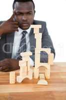 Thoughtful businessman building tower of wooden blocks