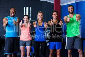Smiling multi-ethnic friends showing thumbs up in gym