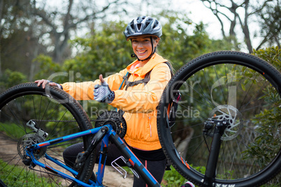 Female biker showing thumbs up while repairing mountain bike